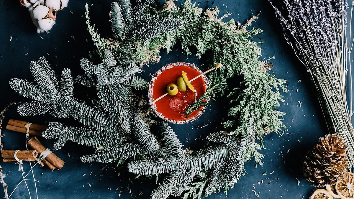 Christmas Bloody Mary with a rosemary sprig and olives, surrounded by evergreen branches