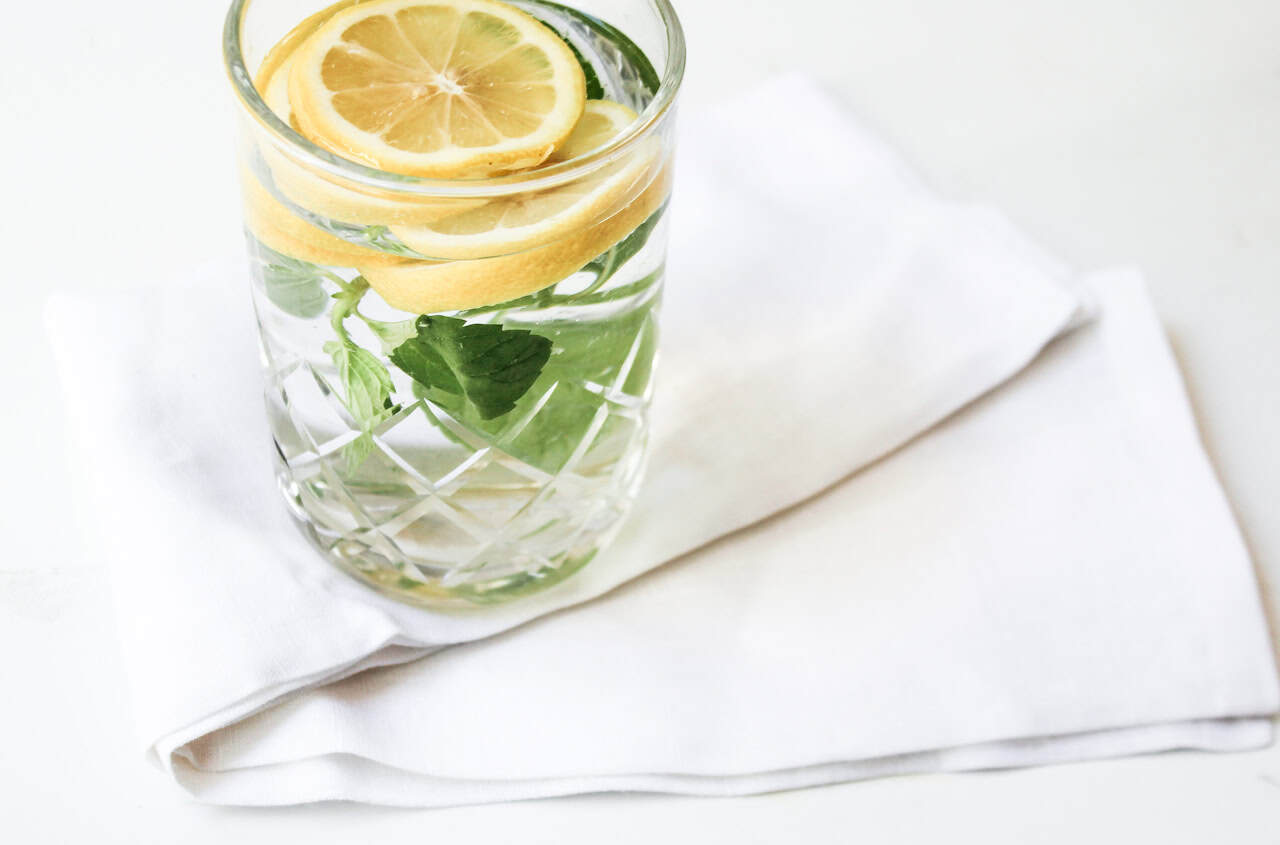 A glass of water with lemon slices and mint leaves, placed on a folded white napkin on a white surface—perfect inspiration for refreshing mocktail recipes.