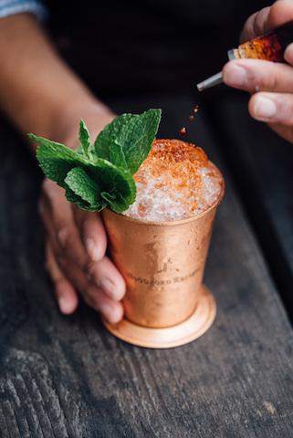 A person pouring a drink into a copper cup.